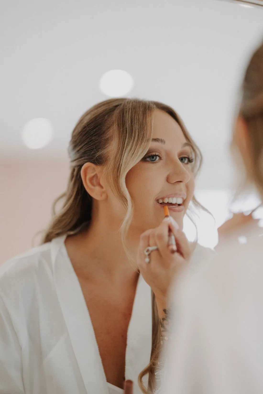 Mariée appliquant son rouge à lèvres face au miroir pendant son maquillage
